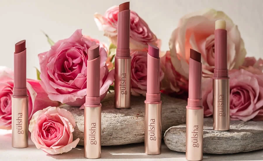 Cuatro pinta labios Gulsha sobre piedra, rodeados de rosas, creando una composición elegante y colorida