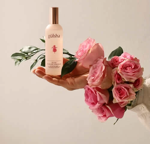 Mano sosteniendo una botella de perfume Gulsha y un ramo de rosas, transmitiendo elegancia y frescura.