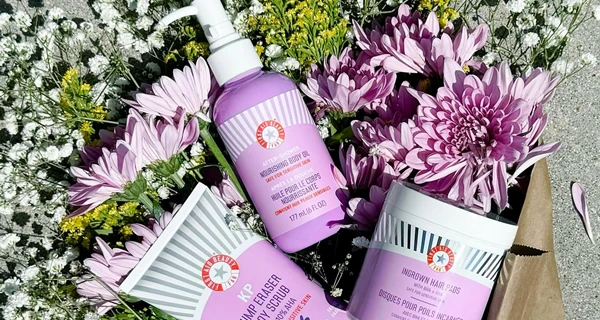 flores junto a una botella de loción corporal de FIRST AID BEAUTY